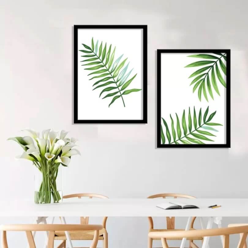Quadros com molduras pretas, em uma parede branca com uma mesa branca e cadeiras cm madeira natural