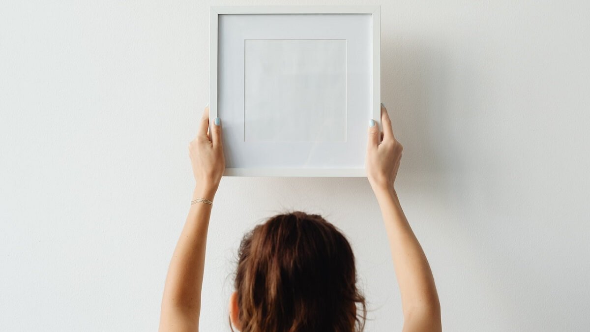 Pessoa pendurando quadro branco em uma parede branca