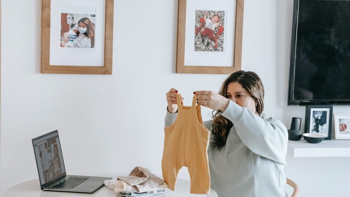 Mãe arrumando roupas do bebê com quadros de fotos do parto na parede